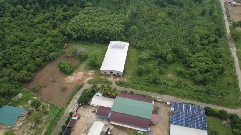 Aerial view of the processing plant: a white-roofed hall, green-roofed buildings and solar panels among trees