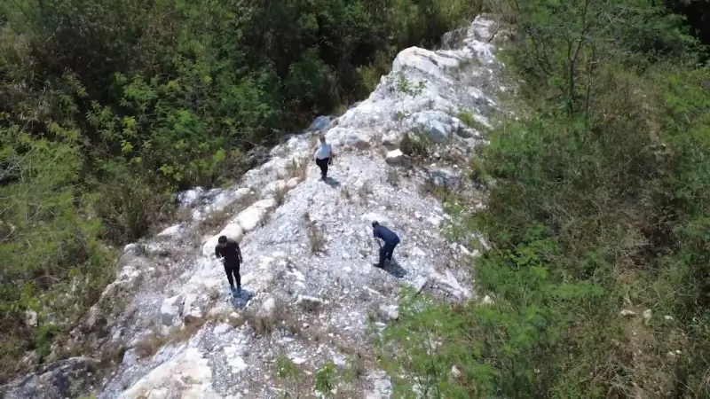 Aerial view of three people standing on a white quartz vein on a hillside